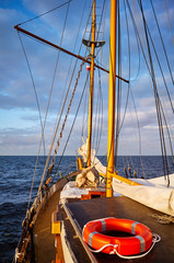 Old sailing ship with a lifebuoy at sunset.