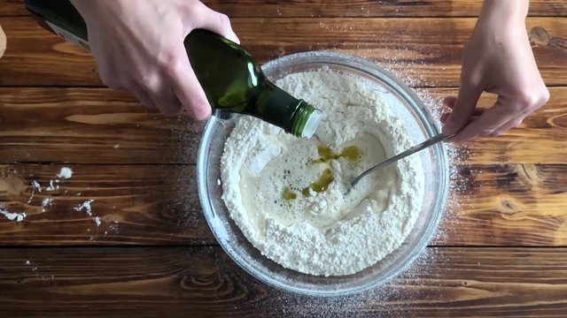 Woman pouring olive oil from bottle to flour, top view video