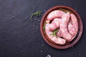 Fresh homemade raw sausages on plate on black textured background.