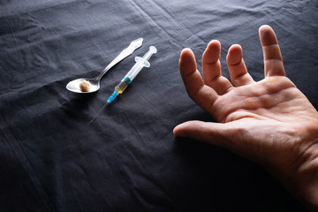 A syringe for injection filled with heroin and a spoon, the hand of an addict