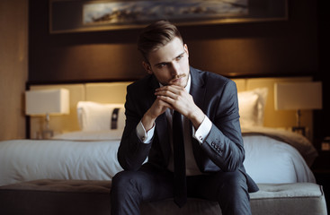 Fototapeta na wymiar Young handsome man relaxing at his apartment in a hotel after business meeting. Business trip. Booking hotel during your vacation. Businessman in luxury room of the expensive beautiful hotel. 