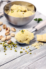 Pistachio ice cream scoop with chopped nuts and white chocolate on a rustic background.