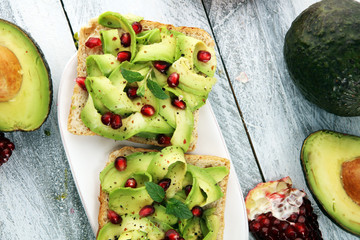 sliced avocado and ripe pomegranates on toast bread with spices and avocado.