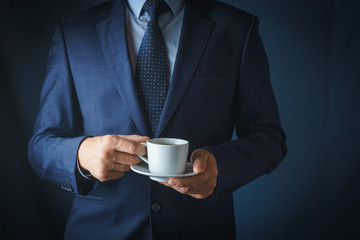 A man in a suit holds a white cup of coffee