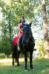 Beautiful brunette in a red costume dancer on a black horseback riding. Overall plan.