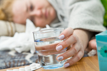 Young woman suffering from headache, cold and flu is holding a glass of water