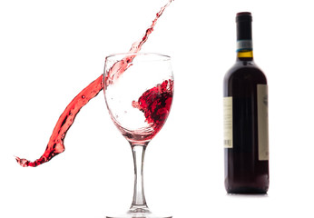 Red wine falls into a glass and creates splash and splashes on a white background.