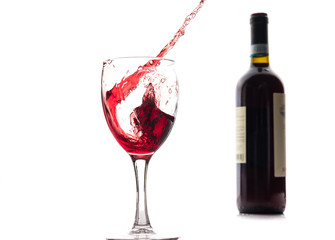 Red wine falls into a glass and creates splash and splashes on a white background.