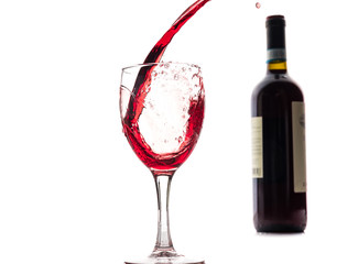 Red wine falls into a glass and creates splash and splashes on a white background.