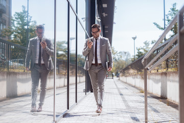 Businessman passing by windows add using smart phone for reading/typing text message. In other hand...