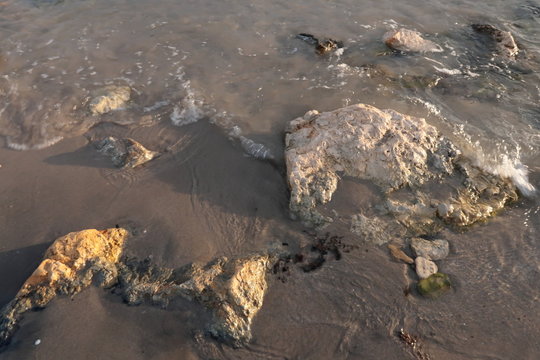 Sea shore with sand and stones and rocks in the water at sunset, close-up