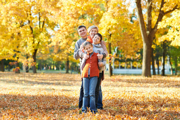 Fototapeta premium Happy family walks in autumn city park. Children and parents posing, smiling, playing and having fun. Bright yellow trees.