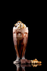 Closeup glass of chocolate milk shake with nuts decorated with whipped cream isolated at black...