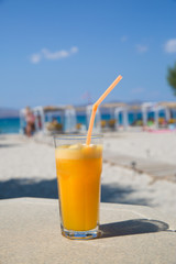 Glass of fresh orange juice on white beach sea view coast background. Relax and vacation concept.