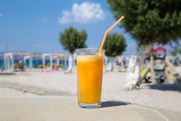 Glass of fresh orange juice on white beach sea view coast background. Relax and vacation concept.