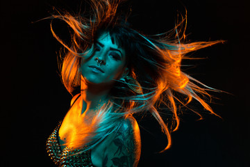 Alternative model with bangs and colored hair poses under teal and orange light wearing a fishnet top