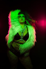 Curvy alternative model with colored hair and fur coat and fishnets under green and pink lighting