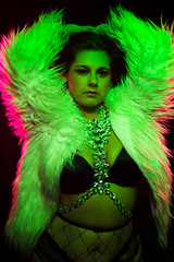 Curvy alternative model with colored hair and fur coat and fishnets under green and pink lighting