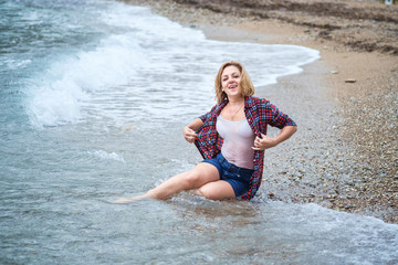 Wet girl sitting in the water on the sea beach after a wave has poured over her