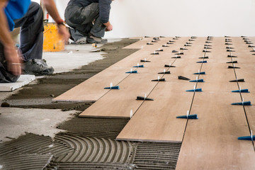 Construction workers laying tile over concrete floor using tile levelers, notched trowels and tile mortar