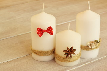 Family holiday. Decorative wax candles tied with thin jute twine and decorated with red bow tie, delicate beige flower and dry flower of an anise on light wooden background