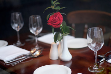 Red rose in a white porcelain vase on a served table in a restaurant
