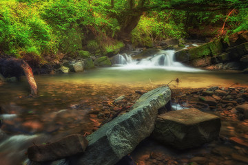 Small waterfall in the forest with big boulders in the foreground