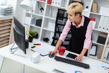 A young girl stands near the Desk in the office and typing on the keyboard.