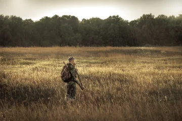 Foto auf Acrylglas Jagd Jäger, der während der Jagdsaison auf dem ländlichen Gebiet in der Nähe von Wäldern bei Sonnenuntergang jagt