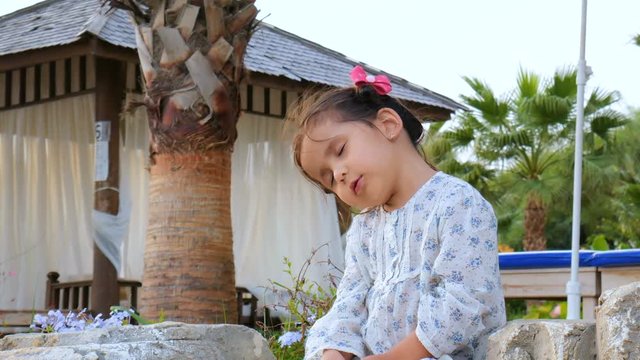 Little actress with a good imagination. Cute beautiful baby girl talking to herself, sitting on the beach under palm trees next to the gazebo.
