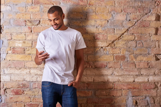 A happy handsome young man using his smartphone in a white tshirt and blue jeans.