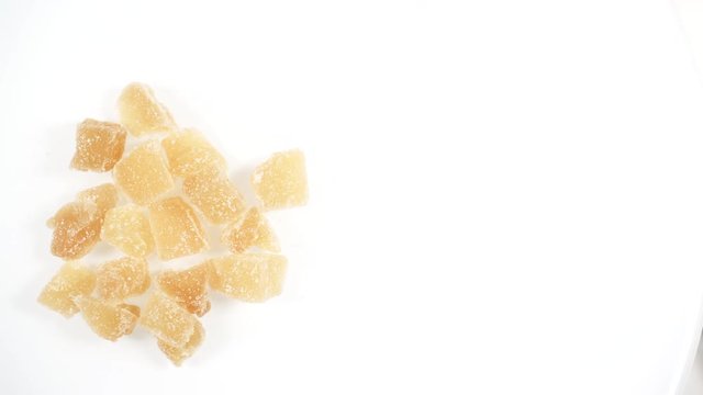Top down view. Heap of crystallized candied ginger pieces rotating on white.  Yummy snack, better alternative to candy