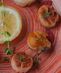 Still life sea scallops on a white plate. With lemon and red pepper. Served on a wooden basis. With oil, garlic and thyme