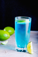 Delicious blue drink with a handful of green lemon. Cocktail with limnom concrete background. Blue cocktail with lemon.