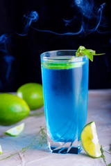 Delicious blue drink with a handful of green lemon. Cocktail with limnom concrete background. Blue cocktail with lemon.