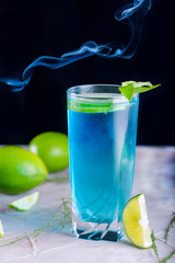 Delicious blue drink with a handful of green lemon. Cocktail with limnom concrete background. Blue cocktail with lemon.