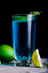 Delicious blue drink with a handful of green lemon. Cocktail with limnom concrete background. Blue cocktail with lemon.