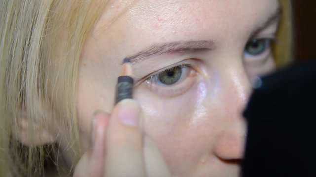 beautiful blonde girl looks in the mirror and paints eyes
