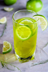 Delicious yellow drink with a handful of green lemon. Cocktail with limnom concrete background. Yellow cocktail with lemon.