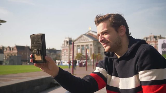 Handsome young man recording a video of him self in Amsterdam with the cellphone in a sunny day. Netherlands. Flat plane