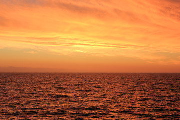 Obraz premium Sunset Sky Landscape Over Calm Sea Water with Vibrant Orange Cloudscape. Beautiful Sky Background at Sunset or Sunrise, Dusk and Dawn Panoramic Skyline View with Still Water on Summer Season Image