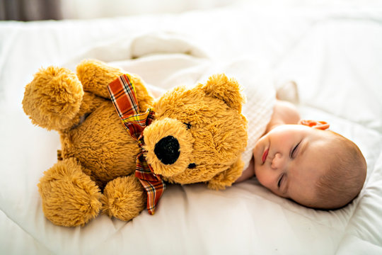 A 4 month baby sleeping on a white bed at home with bear