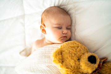 A 4 month baby sleeping on a white bed at home with bear