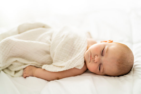 A 4 month baby sleeping on a white bed at home