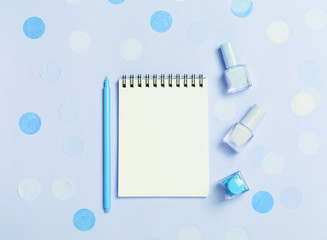 Empty note pad and colorful nail polishes on blue confetti background.