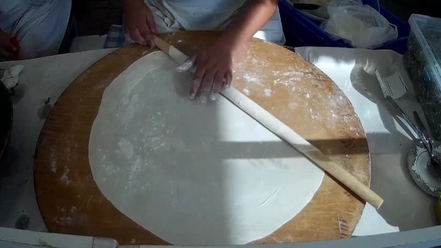 Woman rolling dough extremely thin for gozleme or Turkish pancake.