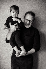 grandfather with beard and glasses with his grandson sitting on his hands