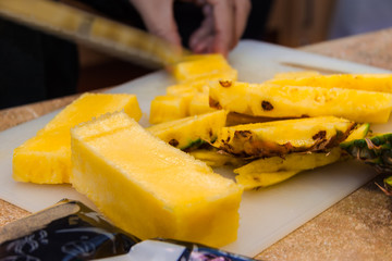 Macro Close Up of Sliced Pineapple Wedges with Hands Slicing in the Background