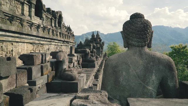 Buddha stone statue on wall of Borobudur temple platform in Java, Indonesia on sunny evening, slide left