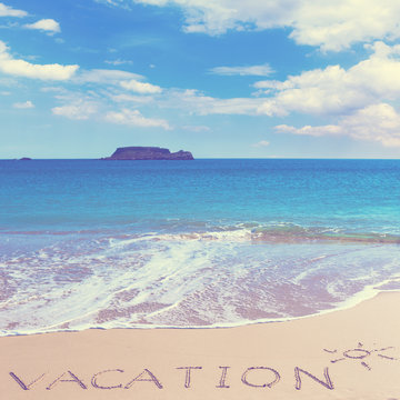 VACATION insctiption under the sun drawing on wet beach sand with the turquoisesea and the island on background